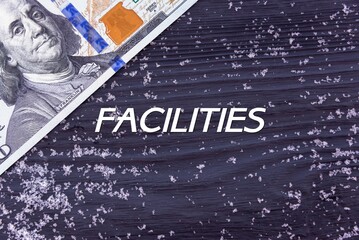 FACILITIES - word (text) on a dark wooden background, money, dollars and snow. Business concept (copy space).