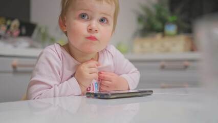 Cute Caucasian Baby Toddler Girl Watching Animated Movie Cartoon on Bright Screen Smartphone 
