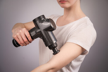 Caucasian woman uses a massager gun for pain in the muscles of the arm.