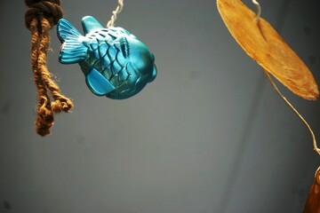 Dekoration mit silber-blauem Plastikfisch am Faden mit hölzernen Blattscheiben vor grauer Wand 