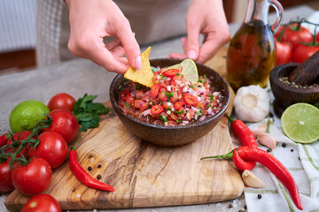 woman dips nacho chip into freshly made salsa dip sauce