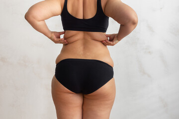 Cropped rearview of fat, adipose, overweight female body in black underwear, checking and holding...
