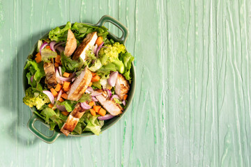Healthy food salad bowl has chicken carrot broccoli on green wood table.