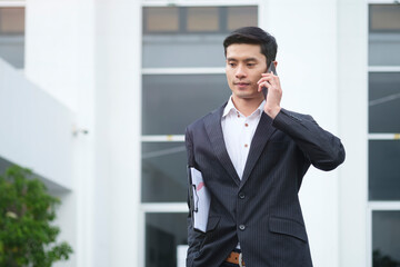 Elegant businessman talking on cell phone while walking outside modern office building.