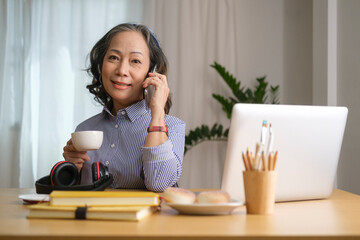 Attractive middle aged woman holding coffee drinking coffee and talking on a cell phone, having pleasant conversation.