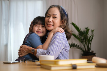 Loving elderly grandma hugging her little granddaughter, enjoying free time on weekend at home together.