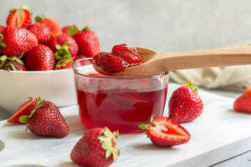 Glass of strawberry jam in wooden spoon on white rustic table