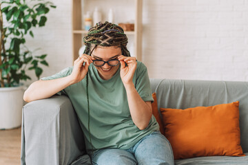 Obraz premium Smiling girl putting on glasses while sitting on the couch.