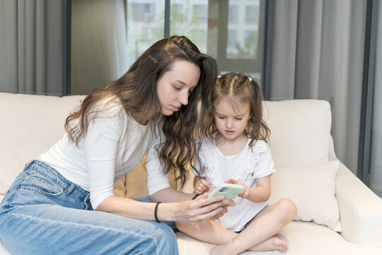 Mom and daughter use smartphone while playing and learning. Technology, internet and children. Parenthood, education, training, free time with children concept.