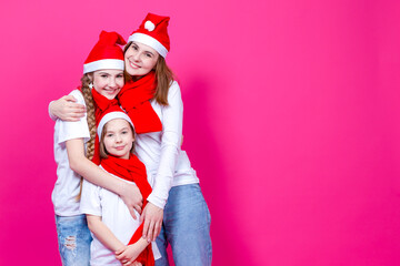 Fototapeta premium Holidays Ideas. Three Happy Caucasian Girls Wearing Santa Hats Having Fun Together While Cuddling To Each Other Over Trendy Vivid Pink Background.