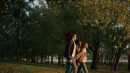 Obraz premium Family walking autumn park holding hands together in evening golden sunlight.