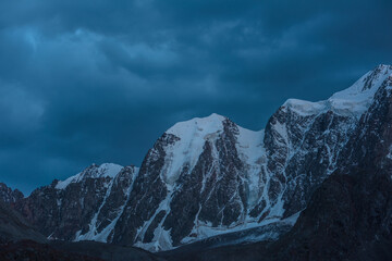 Atmospheric nightly landscape with huge snowy mountain top in dramatic sky. Hanging glacier and cornice on beautiful giant snow mountains in night. High snow-covered mountain range in dusk dim light. - Powered by Adobe