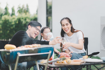 Happy asian family barbecuing and drinking at home outdoor together