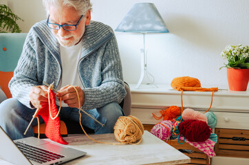 Senior man at home follow online knit tutorial to relax and enjoy resting home leisure activity sitting on the sofa - male people knitting with computer class help - people inner lifestyle hobby - obrazy, fototapety, plakaty