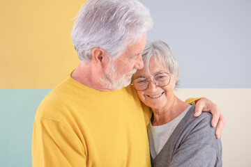 Lovely attractive caucasian senior couple embracing over isolated colorful background. Elderly white-haired man looking at his wife smiling enjoying good company and free time