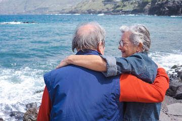 Portrait of happy relaxed senior couple resting on the beach embracing looking each other enjoying vacation or retirement. Horizon over sea