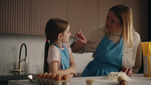 woman is teaching her little daughter to make dough for pizza or pie, mother is kneading flour on table
