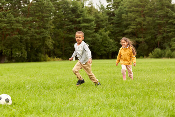 childhood, leisure games and people concept - happy little boy and girl with ball playing soccer at summer park