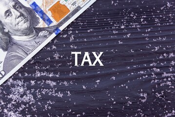 TAX - word (text) on a dark wooden background, money, dollars and snow. Business concept (copy space).