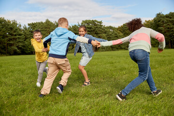 childhood, leisure and people concept - group of happy kids playing round dance at park