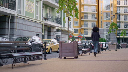 Rear woman walking city stroll empty street alone. Modern residential area.
