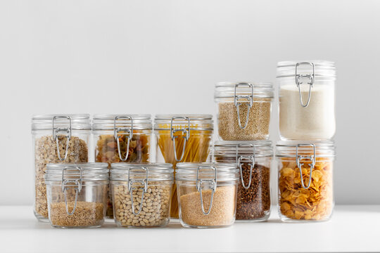 food, culinary and storage concept - jars with different cereals, pasta, beans and cookies on white background