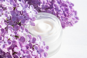 Flowers cosmetic composition with jar of natural face cream and lilac on white background. Organic, plant based beauty products concept. Close up