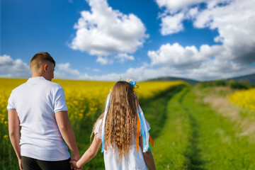 Rear view of children: brother and sister walking far away along path with grass surrounded by yellow fields against sky