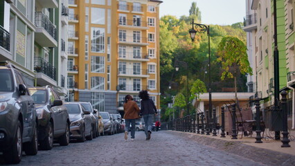 Joyful couple exploring city hold hands rear view. Urban travelers walk street.