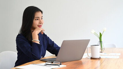 Thoughtful asian businesswoman sitting in office, daydreaming while looking through a window