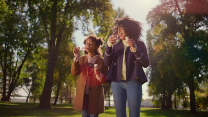 Naklejka premium Joyful family blowing soap bubbles standing in green park. Happy leisure time.