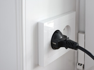 plug from an electrical appliance plugged into an electrical outlet on a light wall background