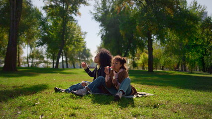 Joyful child mom having fun on family picnic park. Colorful soap bubbles flying.