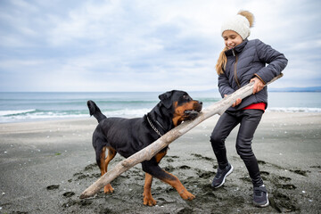 Girl playing with rottweiler dog in cold weather on the beach