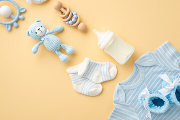 Baby accessories concept. Top view vertical photo of blue shirt knitted booties milk bottle socks wooden rattle knitted teddy-bear toy and teether on isolated pastel beige background