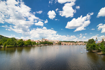 Fototapeta na wymiar Look over Vltava river to Charles bridge, Prague Castle in background under blus sky with white clouds.