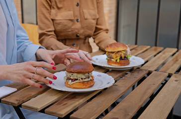 Girlfriends in the restaurant and juicy burgers in their plates. Eat burgers in a good company of like-minded people. Girls are ready to eat delicious burgers. Lunch with a friend