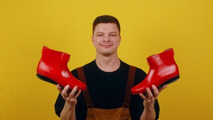 A gardener in overalls holds bright red boots in his hands. The concept of the beginning of the gardening season - Powered by Adobe