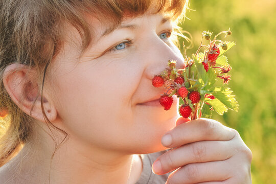 Pretty woman with a bunch of meadow strawberry branches and inhaling its aroma