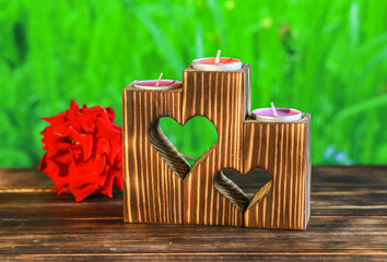 Close-up of wooden candle holders with tea light on red rose petals and blurred green background