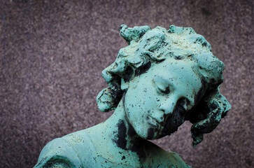Il volto di bronzo ossidato di una bambina triste sopra una tomba del cimitero monumentale di Milano