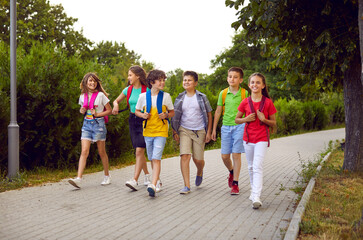 School friendship. Funny schoolchildren group with backpacks have fun walking together on path in...