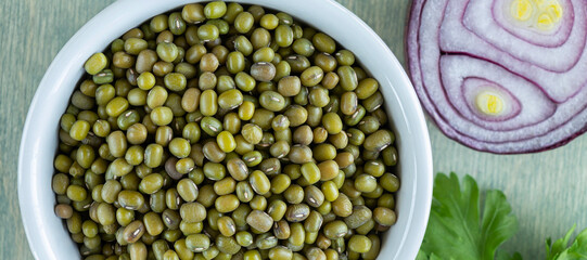 banner with top view on beans of mung sin white plate with onion and parsley. close up mung on a green wooden background. Flat lay.