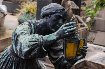 La statua di  bronzo ossidato di una donna con in mano una lampada arancione sopra una tomba del...