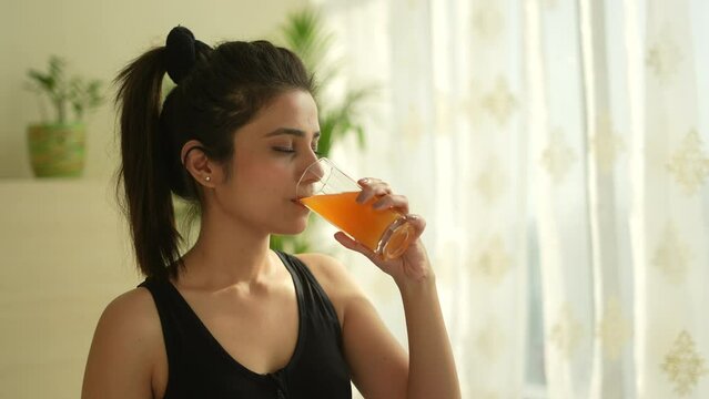 A Beautiful indian woman driking mixed orange juice after yoga.Asian woman doing yoga on yoga met.looking other side  