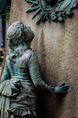 La statua di bronzo ossidato di una bambina sofferente sopra una tomba del cimitero monumentale di...