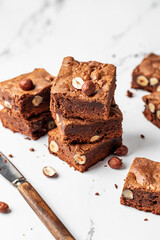 Stack of delicious brownie pieces with hazelnuts on marble background with knife