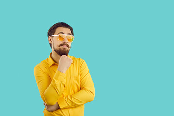 Man with funny expression on his face thinks, imagines or comes up with something interesting. Young caucasian bearded hipster guy holding his chin looking at copy space on light blue background.