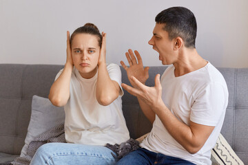 Image of young woman and man having argument, sitting on sofa and screaming, husband screaming and...