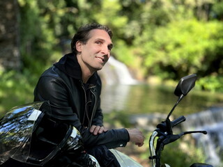male biker sits on a motorcycle against the background of nature and mountain he in a leather jacket on the handlebars of a motorcycle is wearing a helmet. High quality photo